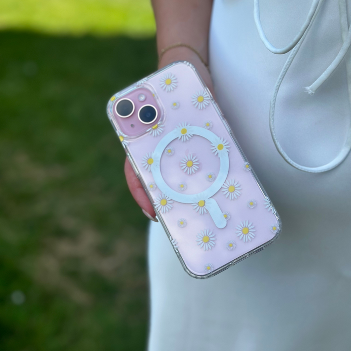Clear MagSafe phone case with daisy pattern held in hand; person in white, blurred grass background.