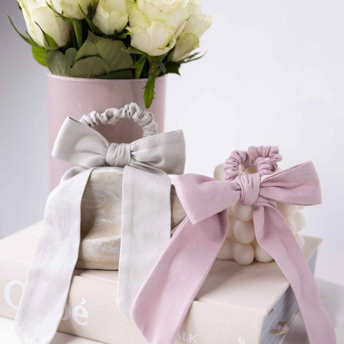 Pumice Stone and Violet Ice Plastic-Free Satin Bows, on a light surface with flowers in the background.