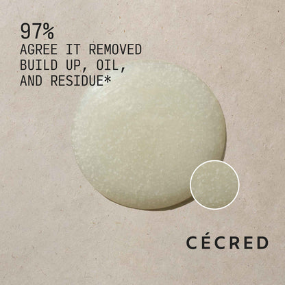 Close-up of Cécred Clarifying Shampoo & Scalp Scrub formula with exfoliating beads and 97% Agree It Removed Buildup, Oil, and Residue claim text against a warm neutral textured background