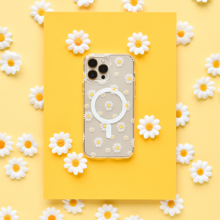 Clear Coconut Lane MagSafe® phone case with white daisy design on yellow paper, surrounded by real daisies.