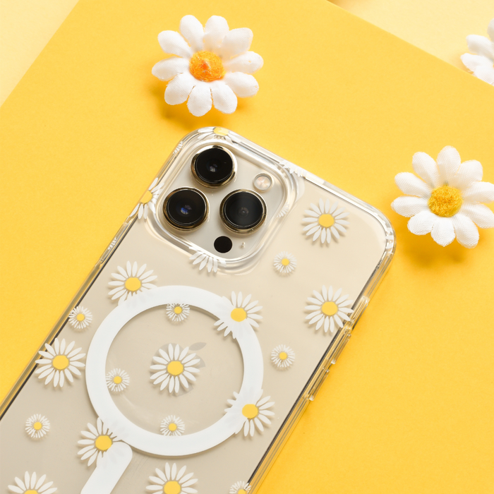 Clear MagSafe phone case with white daisy pattern on an iPhone, shown against a bright yellow background with faux daisies.
