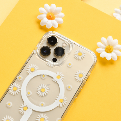 Clear MagSafe phone case with white daisy pattern on an iPhone, shown against a bright yellow background with faux daisies.