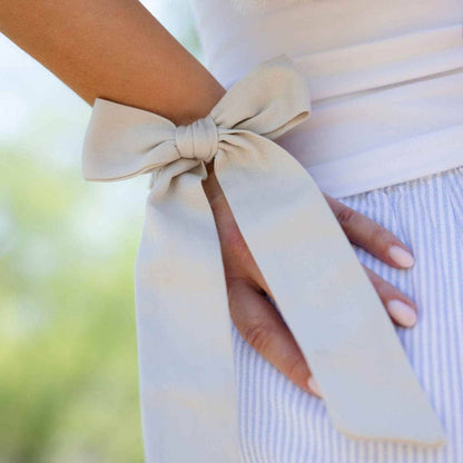Close-up of a person wearing pale linen clothes with kooshoo's stylish satin bow on her wrist.
